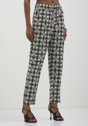 Pantaloni bianchi e neri con un design geometrico, caratterizzati da una vestibilità comoda e una vita elastica. Abbinati a tacchi neri con cinturini.