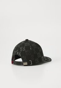 Casquette noire avec un logo "HUGO" répétitif dans des nuances variées. Fabriquée en tissu avec un design structuré et une sangle métallique réglable.