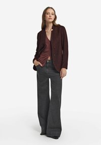 Burgundy dubbelknäppt blazer med texturerad tyg, kombinera med en djup röd topp och vida mörka jeans, accentuerad av släta svarta skor.