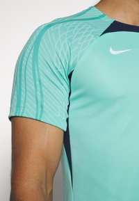 Camiseta deportiva Nike con tejido verde menta y un patrón texturizado en las mangas, además de acentos en azul marino a los lados.