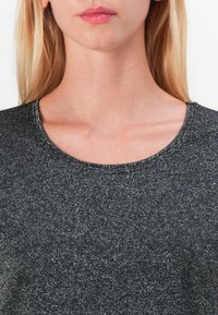 Black short-sleeve top with a round neckline, featuring a fine, sparkly texture and subtle sheen. Seam detailing is visible around the neck.