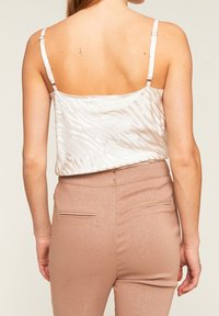 Biała satynowa koszulka na ramiączkach z wzorem w zygzak, z regulowanymi ramiączkami, połączona z błyszczącymi, różowo-złotymi dopasowanymi spodniami z tylnymi kieszeniami i zamkiem.