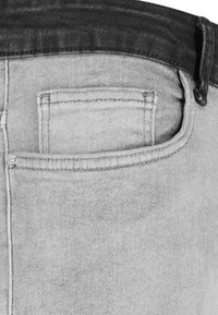 Jeans de denim gris con un diseño clásico de cinco bolsillos, un bolsillo parche en la parte trasera y una cinturilla oscura con detalles de costura visibles.