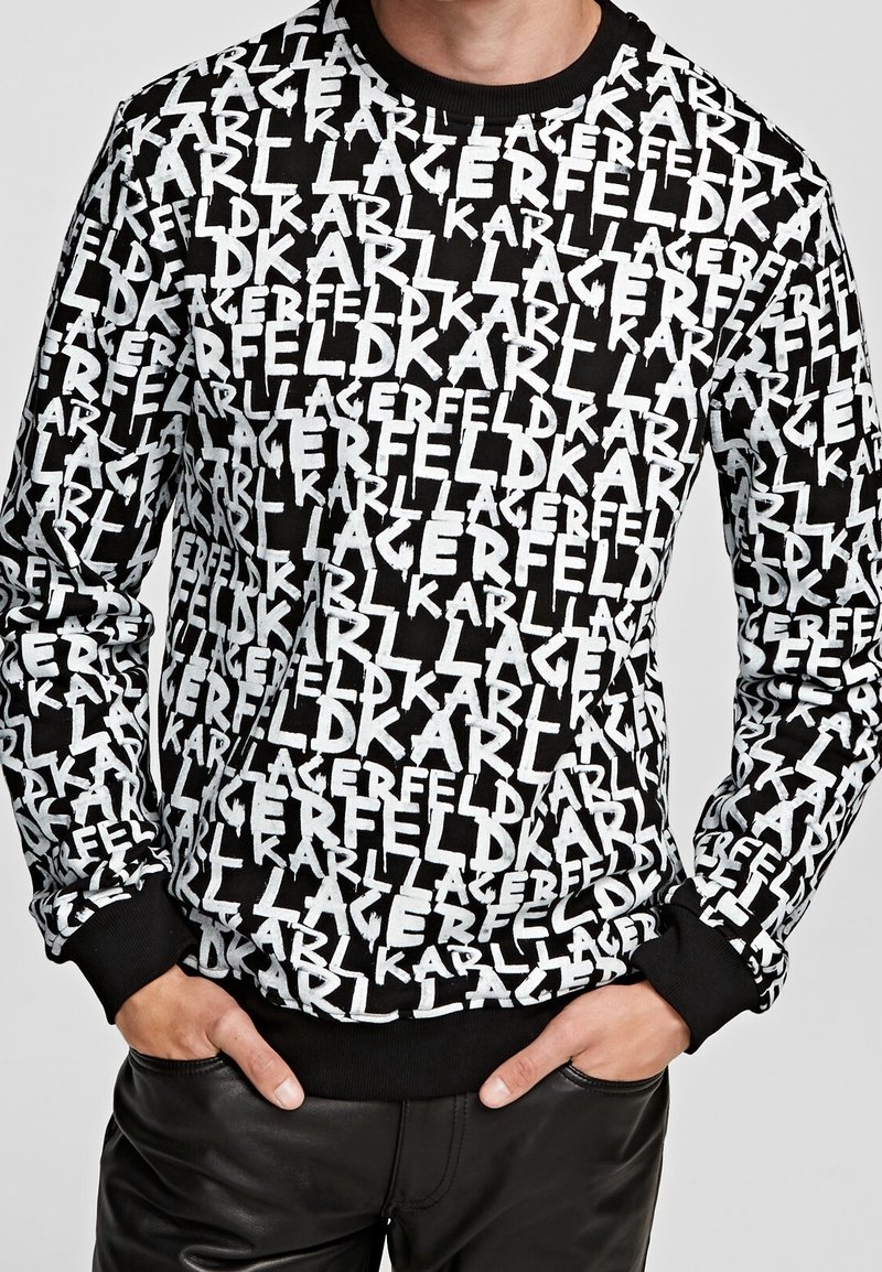 Svart sweatshirt med ett repetitivt vitt textmönster av "Karl Lagerfeld." Ribbad rund hals och muddarna, tillverkad av mjukt material.