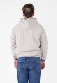 Giacca a vento grigia chiara con cappuccio, dotata di polsini e orlo elasticizzati, realizzata in materiale liscio. Indossata sopra jeans blu, mostra un design semplice e pratico.