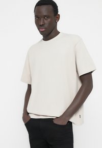 Μπεζ ριγωτό κοντομάνικο μπλουζάκι με στρογγυλή λαιμόκοψη και άνετη γραμμή, σε συνδυασμό με μαύρο τζιν, με ελάχιστες λεπτομέρειες.