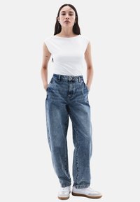 Bílý přiléhavý tričko, džíny s vysokým pasem, volný střih, struktura denimu, délka po kotníky, v kombinaci s bílými teniskami a minimalistickým designem.