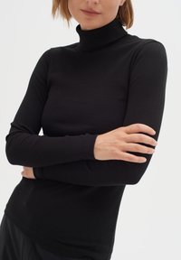 Schwarzes, geripptes Rollkragenoberteil mit langen Ärmeln, enganliegendem Design und weicher Textur. Es hat einen hohen Kragen und enge Bündchen an den Handgelenken.