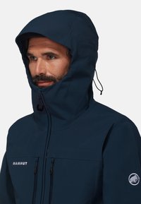 Veste imperméable bleu marine avec un col haut et une capuche réglable, dotée d'une fermeture éclair sur le devant et de deux poches poitrine avec des fermetures éclair contrastées.