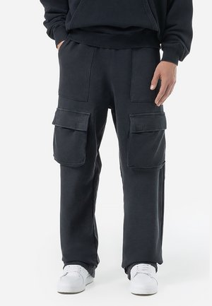 Cargo pants in dark gray fabric, featuring oversized pockets, a relaxed fit, and a smooth texture. Paired with white sneakers.