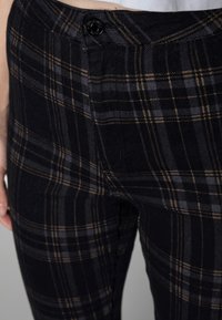 Pantalones de cuadros en negro y gris, fabricados con un tejido texturizado, que cuentan con un botón negro en la cintura y sutiles acentos en marrón en el patrón.