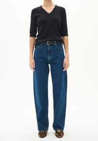 Černý žebrovaný svetr s V-výstřihem, vysoké modré džíny, černý opasek a baleríny s leopardím vzorem. Zaměřeno na pohodlný, uvolněný střih a textura denimu.