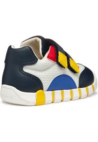 Baskets bleues et blanches avec un dessus texturé, un talon marine, des sangles Velcro jaunes et rouges, et une semelle en caoutchouc avec des accents jaunes.