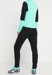Sportswear-set i svart och aqua, med en zip-up topp med hög krage och åtsittande byxor. Outfitten har strukturerad tyg och avsmalnande ben.