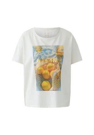 Weißes T-Shirt mit einem Druck von Zitronen in einem Netzbeutel, zwei Weingläsern, einer Flasche und dem Text "APERITIVO AL LIMONE" auf blauem Stoffhintergrund.