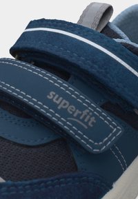 Μπλε παιδικό αθλητικό παπούτσι με λεπτομέρειες από δίχτυ και σουέτ, με δύο ιμάντες Velcro, ο ένας φέρει την ετικέτα "superfit" και γκρι θηλιά στο πίσω μέρος.