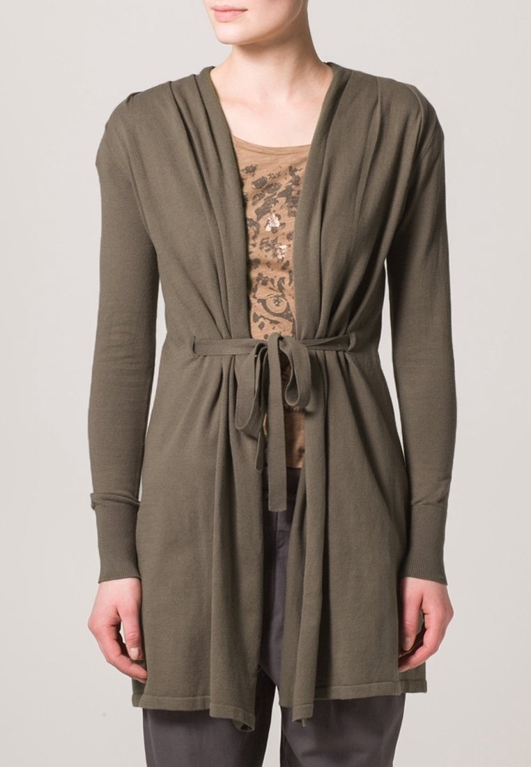 Olivgrön kofta med draperad front och knytband i midjan. Långa ärmar, mjukt tyg och avslappnad passform. Bärs över en mönstrad beige topp.
