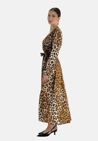 Maxiklänning med leopardmönster, långa ärmar och knyt i midjan, i nyanser av brunt och beige. Bärs med svarta klacksandaler.