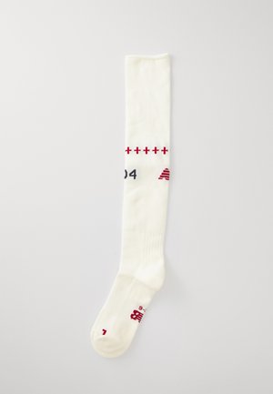 Λευκές κάλτσες ως το γόνατο με ριγωτή υφή, που διαθέτουν διακοσμητικά κόκκινα στοιχεία και αριθμούς, κατασκευασμένες από ελαστικό, αναπνεύσιμο υλικό.