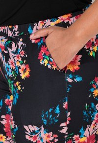 Bloemleggings met een zwarte stof versierd met levendige roze, gele en blauwe bloemenpatronen; bevat een zijzak en een elastische tailleband.
