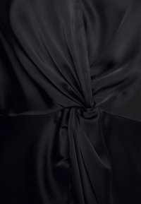 Tissu satin noir torsadé en un nœud central, créant des plis lisses et fluides ainsi qu'une texture brillante.