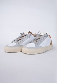 Zapatillas blancas y grises con acabado de gamuza, que cuentan con una suela texturizada, diseño de cordones y detalles en cuero marrón en el talón.