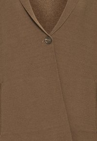 Rudas megztas kardiganas su V formos iškirpte, vienu mygtuku ir dviem priekinėmis kišenėmis. Minkšta tekstūra su subtilia audimo struktūra.