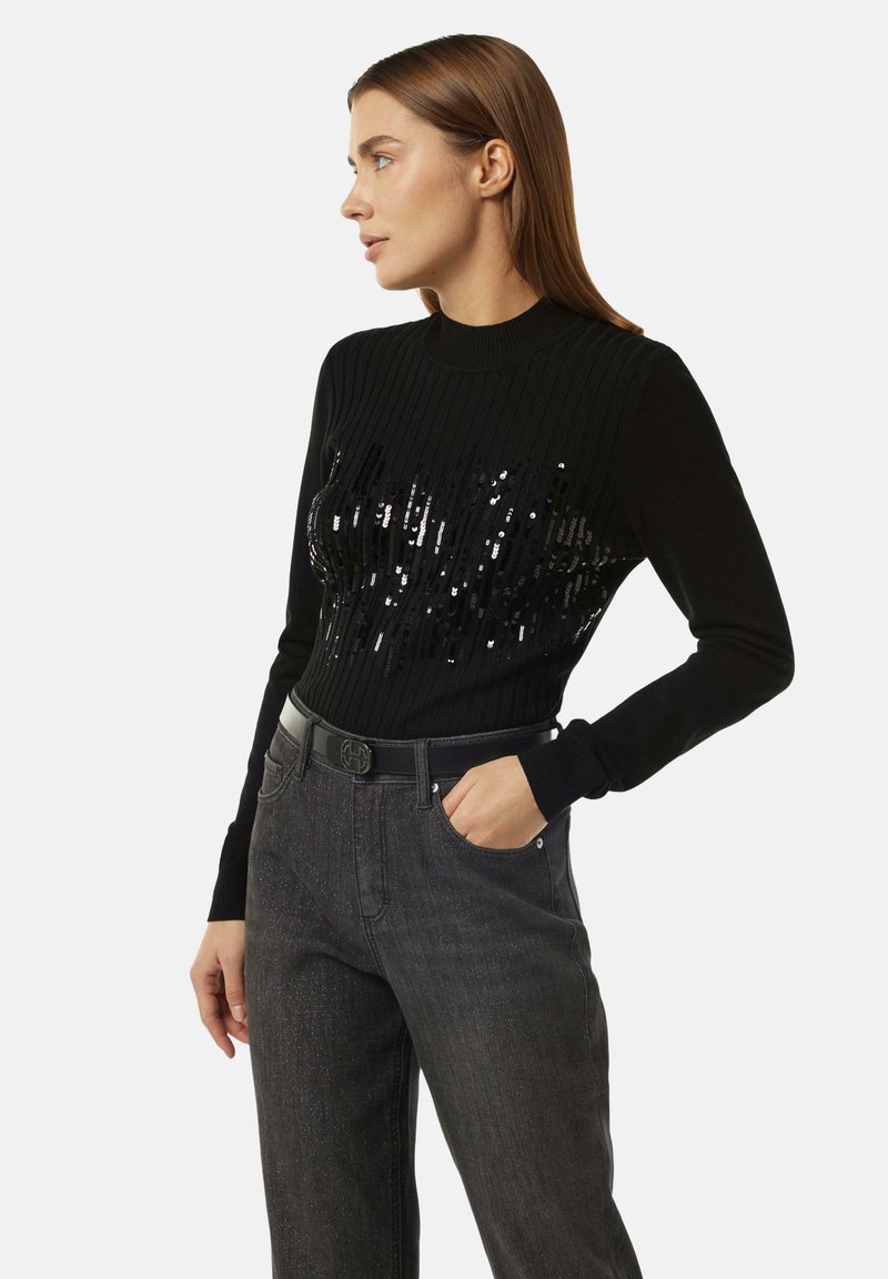 Schwarzer gerippter Pullover mit glitzerndem Design auf der Vorderseite, langen Ärmeln, hohem Kragen, kombiniert mit dunklen Jeans und einem eleganten schwarzen Gürtel.