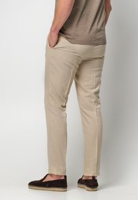 Beżowe lniane spodnie o dopasowanym kroju, z bocznymi kieszeniami i gładką fakturą. W połączeniu z ciemnobrązowymi butami wsuwanymi.