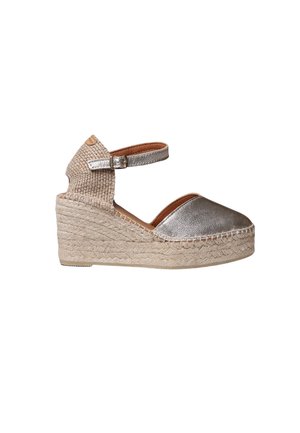 Strieborná kovová espadrilová platforma s tkaným textilným zvrškom, remienkom na členok a spletenou stielkou z jutového vlákna. Zaoblená špička a textúrované detaily.
