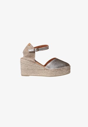 Strieborná kovová espadrilová platforma s tkaným textilným zvrškom, remienkom na členok a spletenou stielkou z jutového vlákna. Zaoblená špička a textúrované detaily.