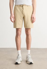 Shorts de color beige con textura, cintura elástica con cordón, bolsillos frontales y diseño ajustado, combinados con calcetines blancos y zapatillas grises.