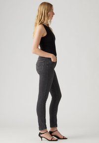 Top negro sin mangas combinado con jeans ajustados de talle alto en gris oscuro y sandalias de tacón negro. Diseño minimalista con líneas limpias.