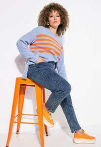 Suéter azul claro con rayas naranjas, jeans azules y zapatillas naranjas. El conjunto presenta texturas variadas y un ajuste relajado.