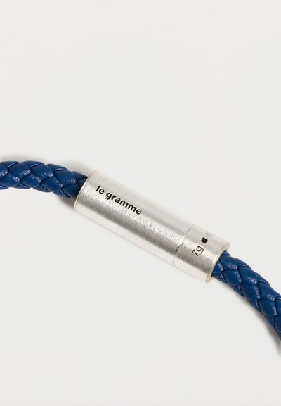 Bracelet en cuir tressé bleu avec un fermoir cylindrique en argent gravé de "le gramme" et de la mention du poids "7g".