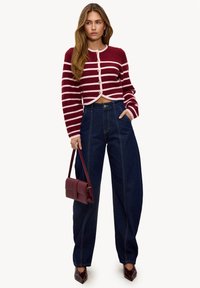 Cárdigan corto a rayas rojas y blancas con detalles de botones, combinado con vaqueros azules de pierna ancha de tiro alto. Los accesorios incluyen un bolso burdeos.