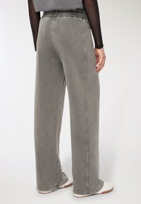 Osoba w luźnych szarych spodniach o wysokim stanie z elastycznym pasem, połączonych z białymi sneakerami i czarną bluzką z długim rękawem.