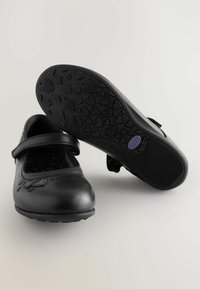 Schwarze Leder-Mary-Jane-Schuhe mit einem Riemen, runder Zehenform und strukturiertem schwarzem Außensohle mit Herzmustern. Das Innenfutter hat ein bedrucktes Design.
