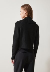 Must must cropped-sweater tekstureeritud kudumisest, laia ribaga krae ja äärega. Seljaosas on sobivad varrukad ja puhas joon.