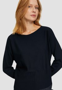 Navy knitted sweater with a wide neckline, ribbed hem, and long sleeves, featuring a smooth texture and relaxed fit.