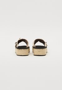 Sandali espadrillas con suola piatta nera, parte superiore in juta intessuta beige e cuciture nere. La parte posteriore presenta una fascia per una vestibilità sicura.