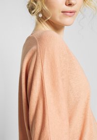 Maglione color pesca chiaro realizzato in un tessuto morbido e testurizzato, con una vestibilità rilassata e spalle scese. Design semplice e minimale.