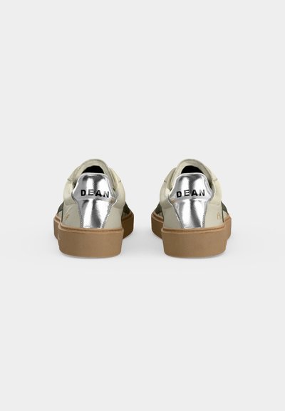 Paire de baskets beige avec semelles marron clair et languettes métalliques argentées au talon étiquetées "DEAN" montrées de dos sur fond blanc.