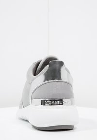 Szare buty sportowe z siateczkową cholewką i błyszczącymi srebrnymi akcentami, z wyściółką w pięcie i teksturowaną białą podeszwą. Obecne logo marki.