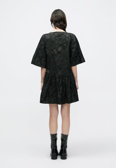 Μαύρο φόρεμα με κοντά μανίκια, σούρα στη μέση και υφή υφάσματος. Φορεμένο με μαύρα μποτάκια αστραγάλου με πλαϊνό φερμουάρ.