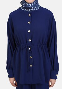 Navyblauw button-up shirt met een gestrikt middel, lange mouwen, gouden knopen, geplooide details en een ronde halslijn.