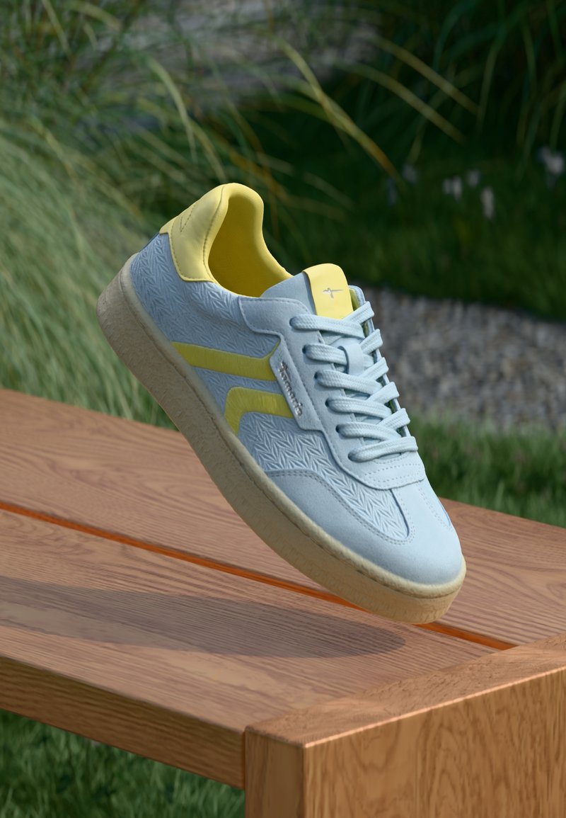 Helleblaue Sneaker mit gelben Akzenten, strukturierten Oberflächen, weißer Außensohle und grauen Schnürsenkeln. Abgerundete Zehenpartie und Low-Top-Design.