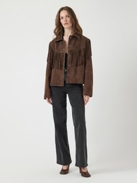 Veste en daim marron avec des franges sur les épaules, associée à un jean noir et des talons marron. Texture lisse, design décontracté, fermeture boutonnée à l'avant.