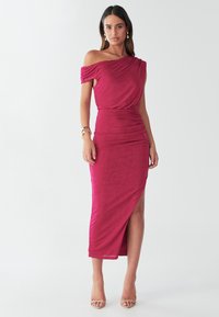 Fuksija haljina s otkrivenim ramenima, krojena s naborima sa strane, prorez do koljena i meka tekstura; stilizirana s neutralnim sandalama i modnim dodacima.