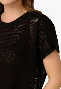 Černý pletený top s volným střihem, síťovým vzorem, krátkými rukávy a širokým výstřihem. Měkká textura a otevřený úplet.